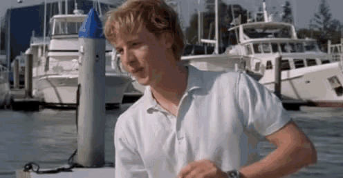 a man in a white shirt is standing in front of a marina with boats .