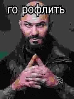 a man with a beard and a watch is sitting with his hands folded in front of him .