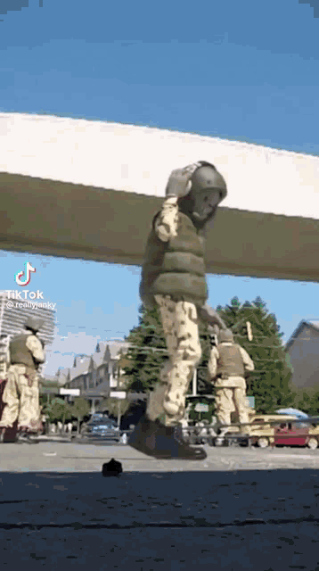 a group of soldiers are standing under a bridge and one of them is wearing a helmet .