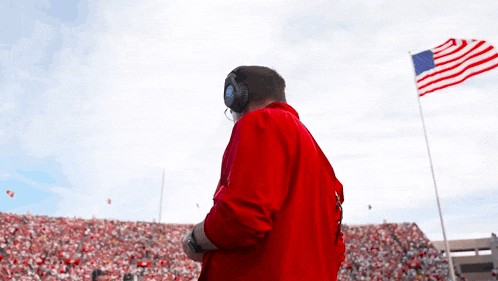 a man in a red jacket stands in front of a large american flag