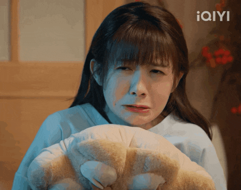a woman is holding a teddy bear with the iqyi logo in the background