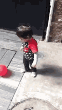 a little boy is standing on a sidewalk next to a red balloon .