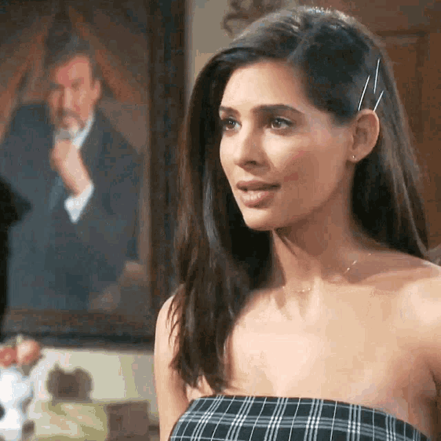 a woman in a plaid top is standing in front of a painting of a man