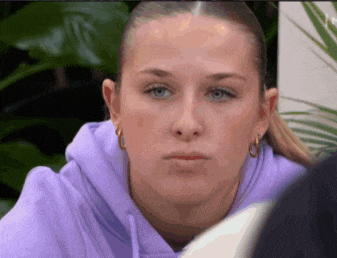 a woman wearing a purple hoodie and hoop earrings is looking at the camera