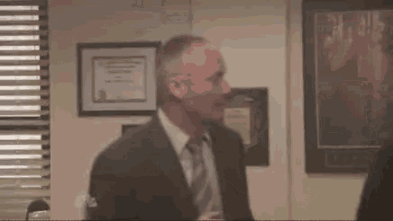 a man in a suit and tie is talking to another man in an office