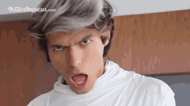 a man with gray hair and a white shirt is making a funny face with his tongue out .