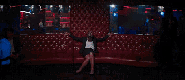 a woman in a suit sits on a red couch