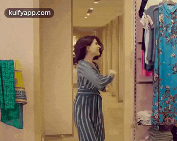 a woman in a striped dress is standing in a closet with clothes hanging on the wall .