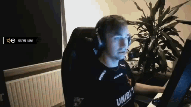 a man wearing headphones and a shirt that says unibet is sitting in front of a computer screen .