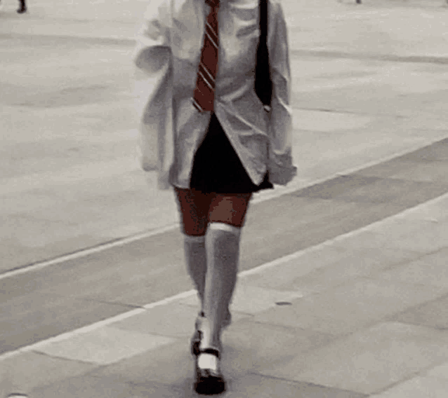 a woman wearing knee high socks and a tie is walking down the street .