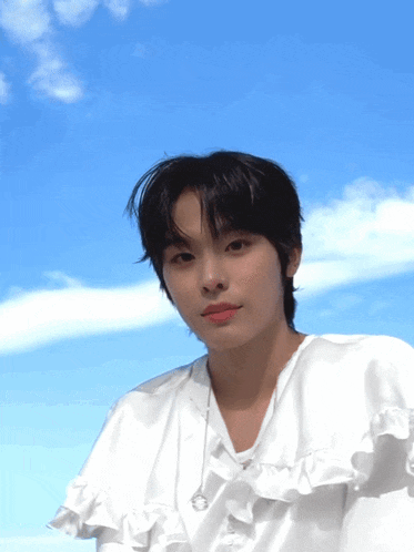 a young man wearing a white shirt with ruffles and a blue sky behind him