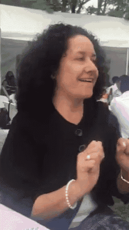a woman with curly hair wearing a black shirt and pearl bracelet is smiling