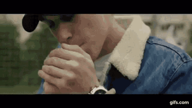 a man in a denim jacket is smoking a cigarette while wearing a watch .
