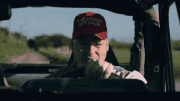 a man in a make america great again hat is driving a vehicle