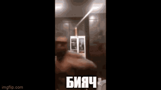 a man without a shirt is standing in front of a mirror in a room with russian writing on it .