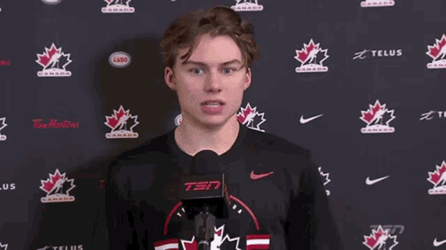 a young man is talking into a microphone in front of a wall that says canada on it