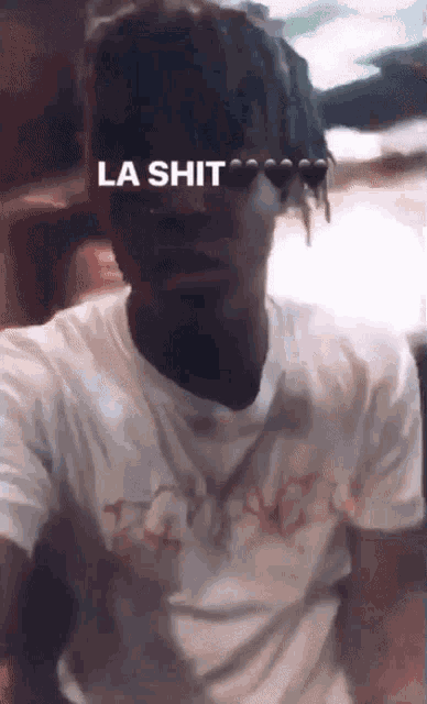 a man with dreadlocks is wearing a t-shirt that says ' la shit ' on it