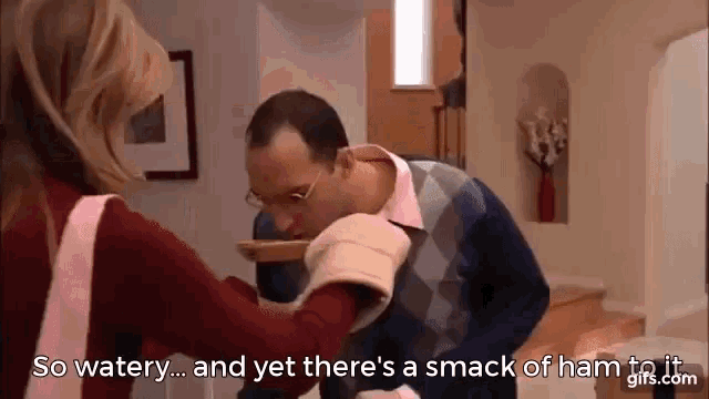 a woman is feeding a man a smack of ham to his face .