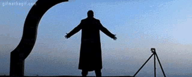 a silhouette of a man with his arms outstretched standing next to a tripod .