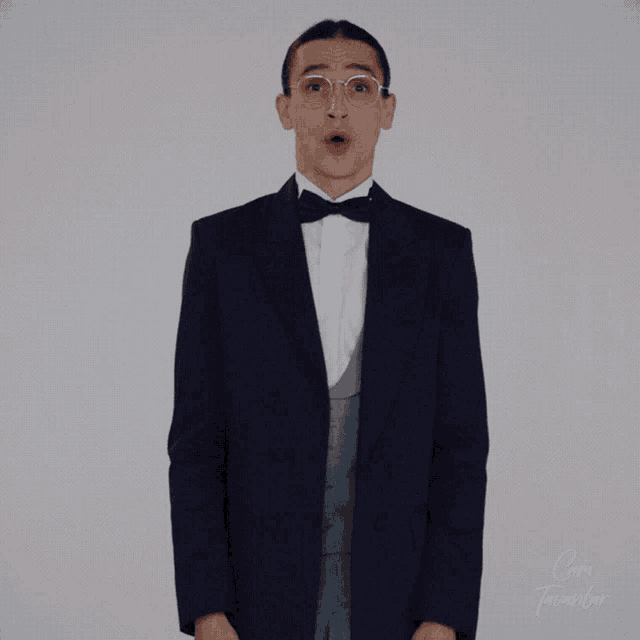 a man in a tuxedo and bow tie is standing in front of a sign that says com tavanlor