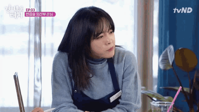 a woman in a blue sweater is sitting at a table with a cup of coffee and chopsticks ..