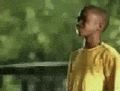 a young boy in a yellow shirt is standing in front of a tree .