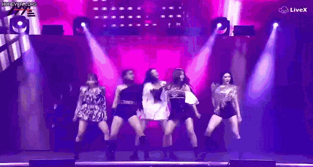 a group of young women are dancing on a stage in front of a pink background .