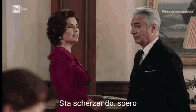 a woman in a red dress stands next to a man in a suit and tie with the words sta scherzando spero written below them