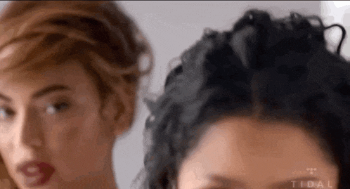 two women are standing next to each other and looking at the camera . one of the women is wearing red lipstick .
