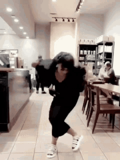 a woman in a black dress and white shoes is dancing in a coffee shop