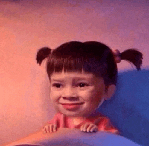 a little girl with pigtails is smiling while sitting on a bed .