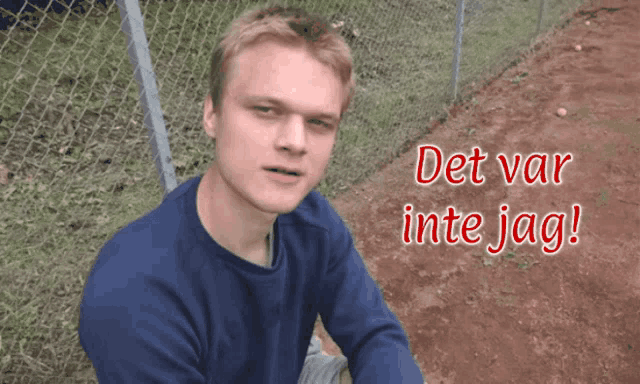 a man in a blue shirt sits in front of a fence with the words det var inte jag