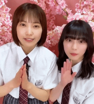 two girls in school uniforms and ties are standing next to each other in front of cherry blossom trees .