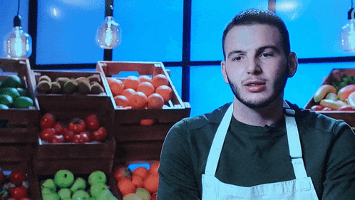 a man wearing an apron stands in front of crates of fruit