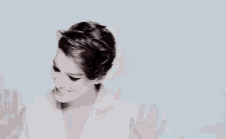 a woman with short hair is smiling and waving her hands in front of a blue background .