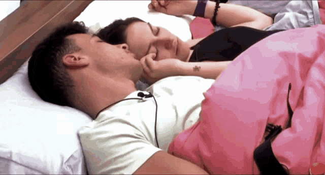 a man and a woman are sleeping in a bed with pink sheets
