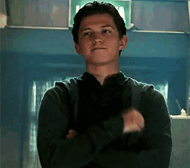 a young man in a black sweater is standing with his arms crossed in a room .