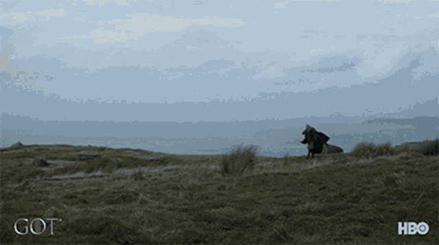 a man in a cape is standing in a field with the word got on the bottom