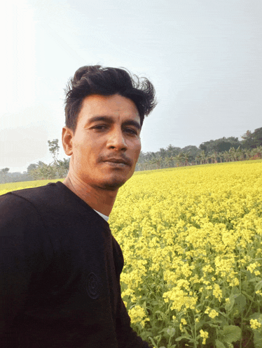 a man stands in front of a field of yellow flowers with a black shirt on