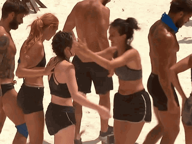a group of people are standing on a beach and one of them is wearing a bandana around his neck