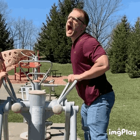 a man in a maroon under armour shirt is yawning while using an exercise machine