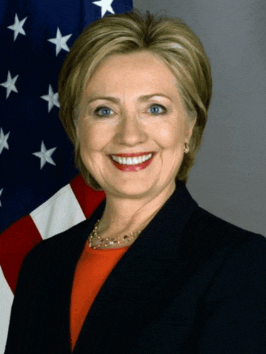 hillary clinton smiles in front of a flag