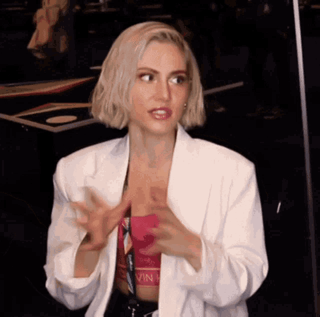 a woman with blonde hair is wearing a white jacket and a pink tank top .