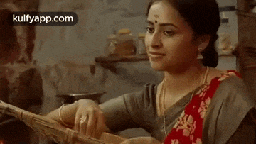 a woman in a saree is playing a musical instrument .