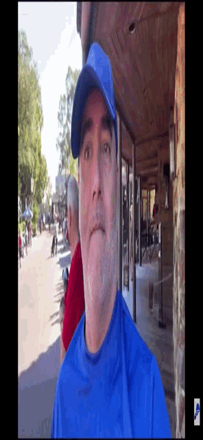 a man wearing a blue hat and a blue shirt stands in front of a wooden building