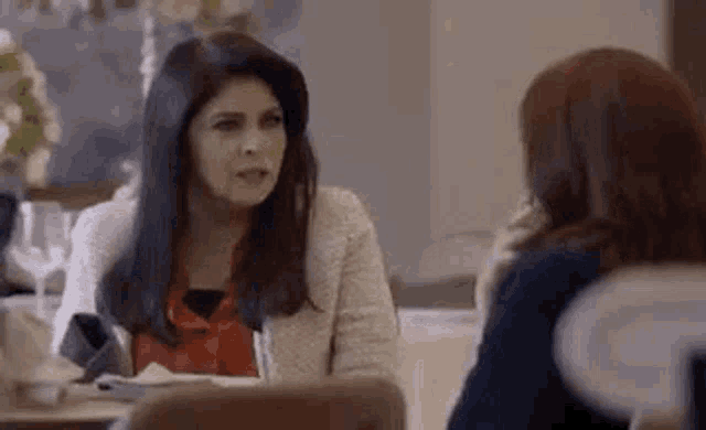 two women are sitting at a table having a conversation .
