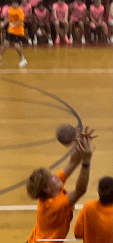 a man in an orange shirt is jumping to catch a basketball on a basketball court