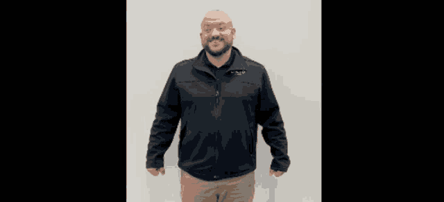 a bald man with a beard wearing a black jacket is smiling