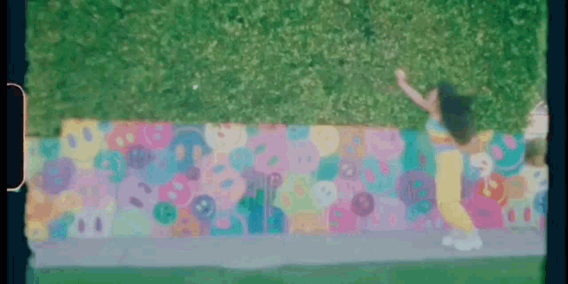 a girl is standing on a sidewalk next to a colorful mural .