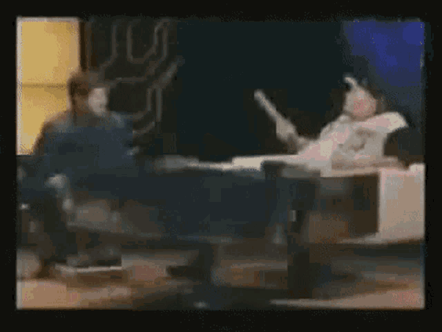 a man is sitting at a table talking to another man in a room .